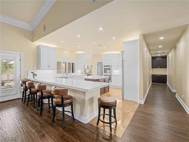 kitchen with a breakfast bar area, a peninsula, ornamental molding, light countertops, and double oven