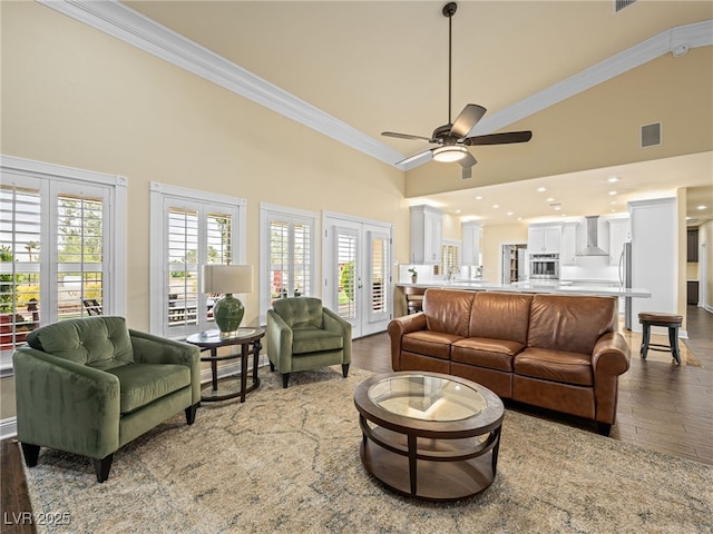 living area featuring visible vents, high vaulted ceiling, wood finished floors, and ornamental molding