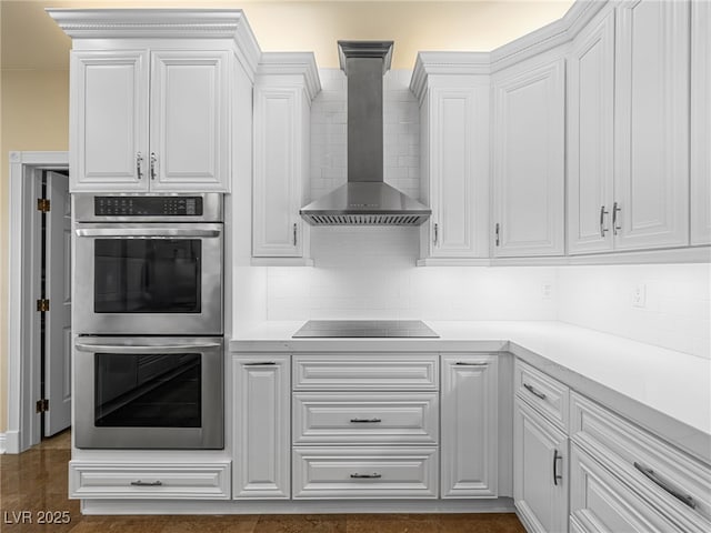 kitchen with stainless steel double oven, black electric cooktop, wall chimney exhaust hood, and white cabinets