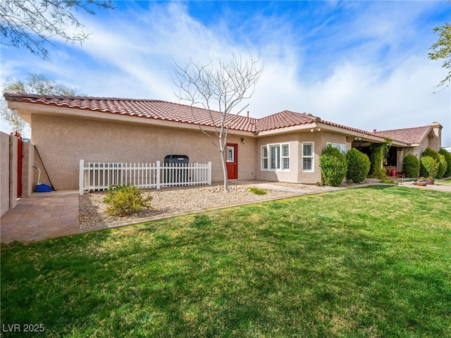 back of property with a tile roof, stucco siding, a lawn, and fence