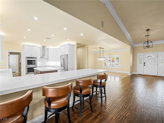 kitchen featuring ornamental molding, stainless steel appliances, wall chimney exhaust hood, and dark wood-style flooring