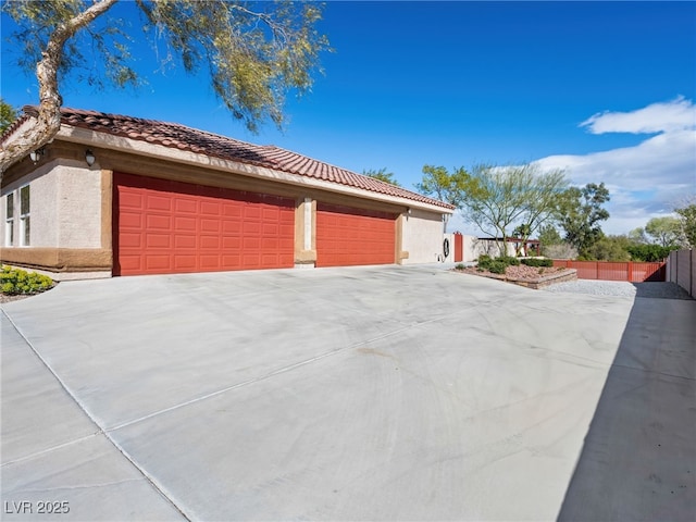 view of home's exterior with a tiled roof, fence, driveway, and stucco siding