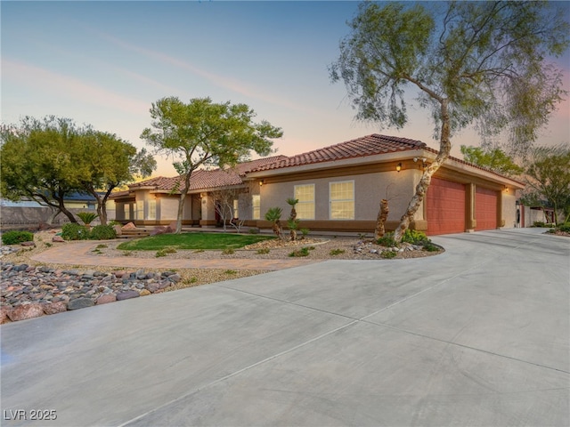 mediterranean / spanish house featuring stucco siding, driveway, a tile roof, and a garage