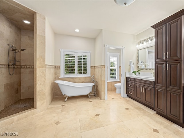 full bathroom featuring walk in shower, a freestanding bath, toilet, vanity, and tile walls