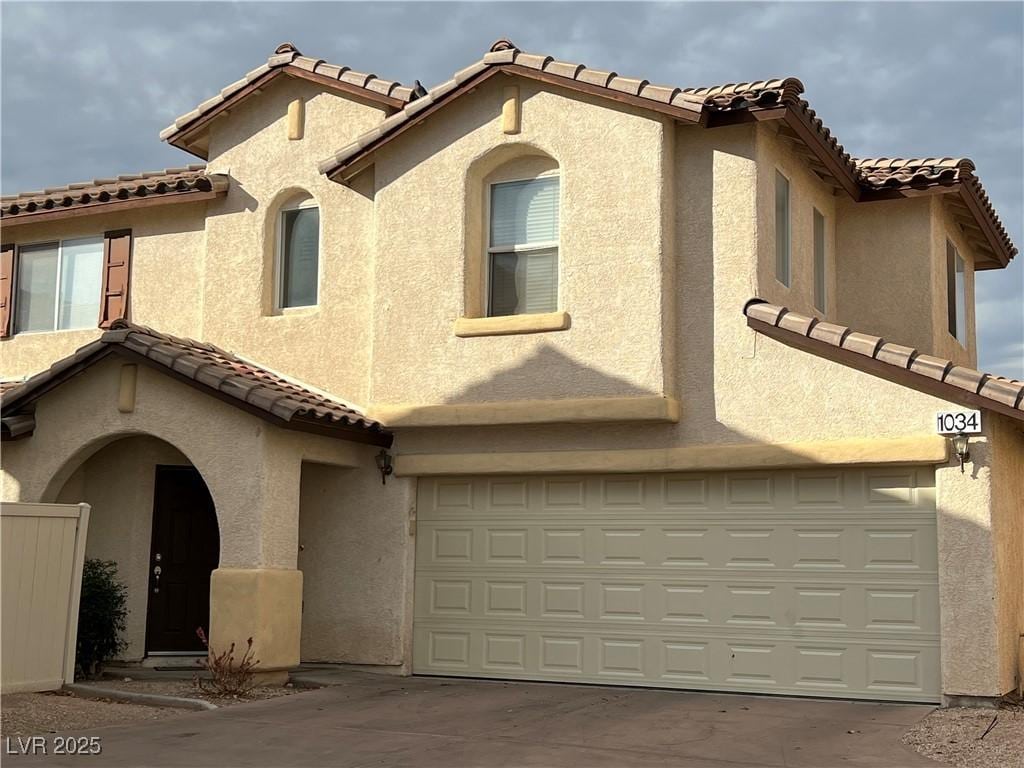 mediterranean / spanish-style home with a garage, a tiled roof, concrete driveway, and stucco siding