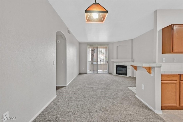 unfurnished living room with visible vents, arched walkways, a fireplace, baseboards, and light colored carpet