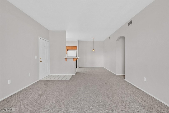 unfurnished living room featuring arched walkways, visible vents, light carpet, and baseboards