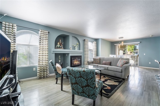 living room with a textured ceiling, wood finished floors, a glass covered fireplace, and baseboards