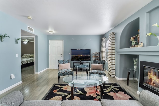 living area featuring a glass covered fireplace, visible vents, baseboards, and wood finished floors