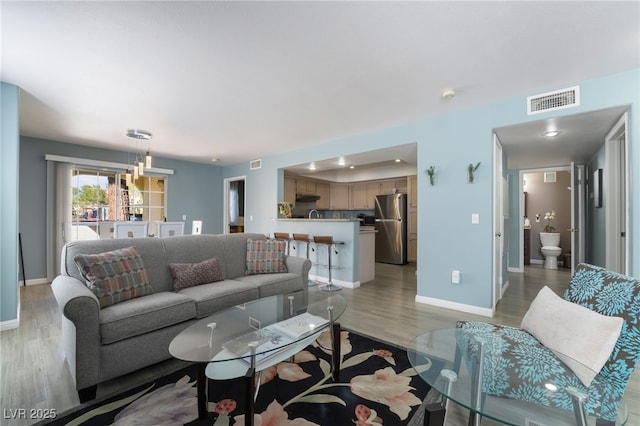 living room with light wood-style flooring, visible vents, and baseboards