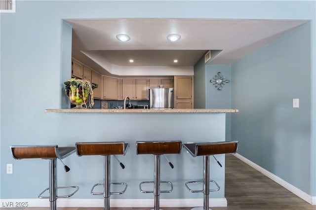 kitchen with visible vents, a kitchen breakfast bar, freestanding refrigerator, a peninsula, and light countertops