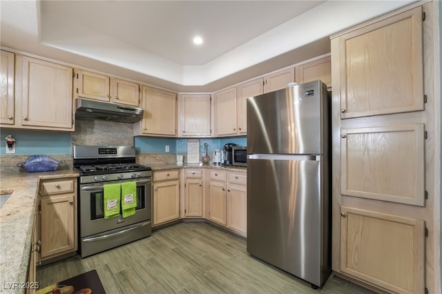 kitchen with a raised ceiling, appliances with stainless steel finishes, light brown cabinets, and under cabinet range hood