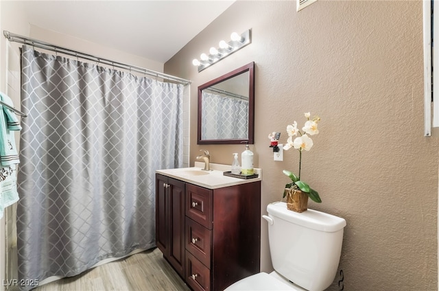 full bathroom featuring a textured wall, a shower with shower curtain, toilet, vanity, and wood finished floors