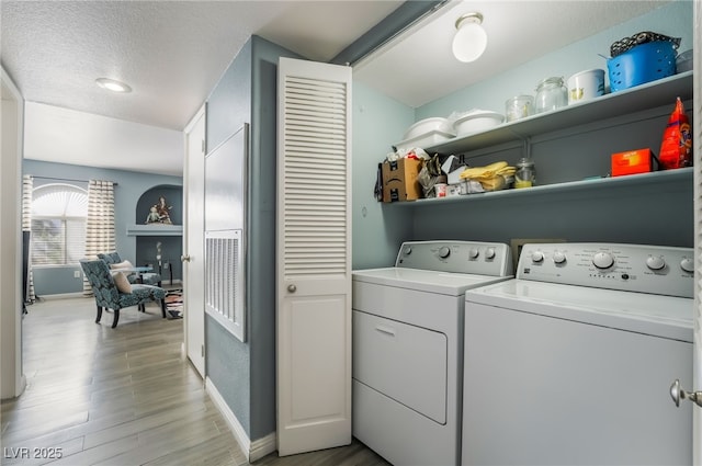 washroom with a textured ceiling, light wood-style flooring, laundry area, separate washer and dryer, and baseboards