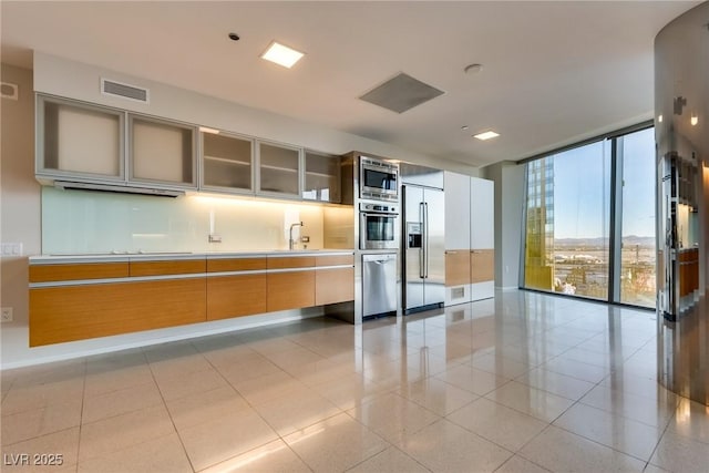 kitchen featuring built in appliances, visible vents, a wall of windows, modern cabinets, and glass insert cabinets