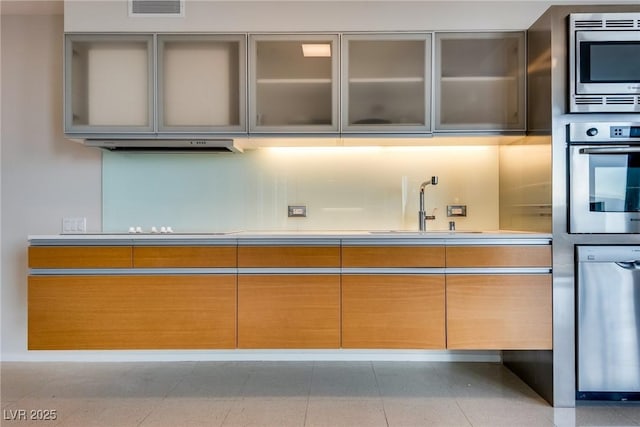 kitchen featuring visible vents, appliances with stainless steel finishes, glass insert cabinets, a sink, and under cabinet range hood