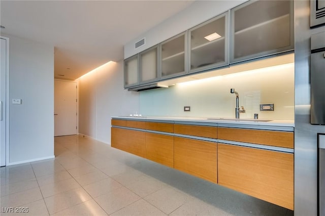 kitchen with light tile patterned floors, a sink, visible vents, light countertops, and glass insert cabinets