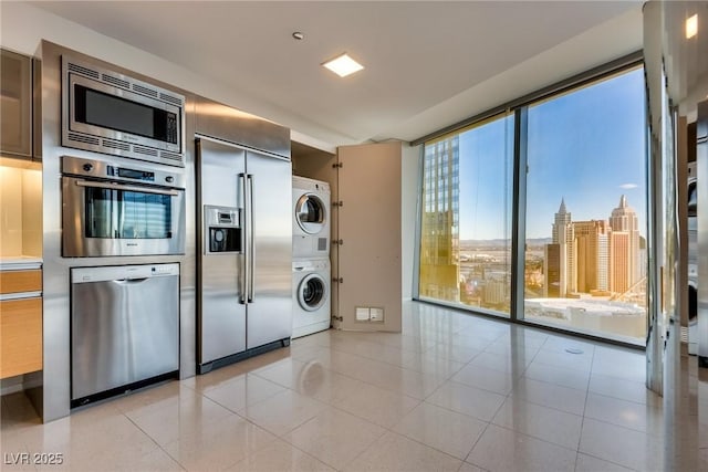 kitchen with light tile patterned floors, stacked washer and clothes dryer, built in appliances, a view of city, and expansive windows