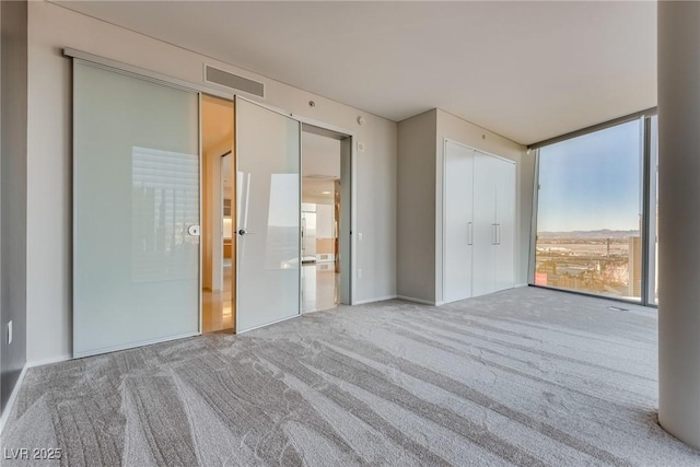 carpeted spare room featuring floor to ceiling windows and visible vents