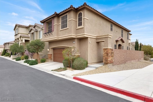 mediterranean / spanish house featuring an attached garage, fence, a tile roof, driveway, and stucco siding