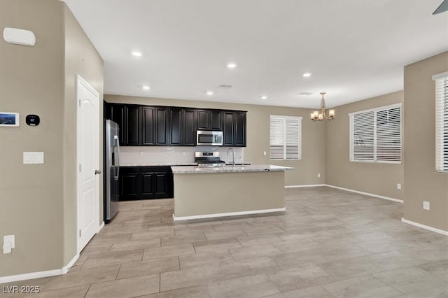 kitchen featuring stainless steel appliances, recessed lighting, an island with sink, a chandelier, and baseboards