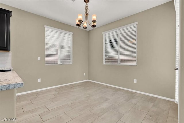 unfurnished dining area featuring baseboards and an inviting chandelier