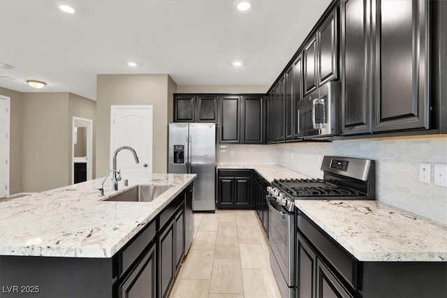 kitchen with tasteful backsplash, appliances with stainless steel finishes, dark cabinets, a kitchen island with sink, and a sink