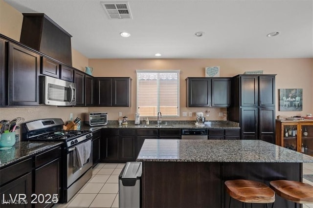 kitchen with visible vents, appliances with stainless steel finishes, a kitchen breakfast bar, dark stone countertops, and a sink