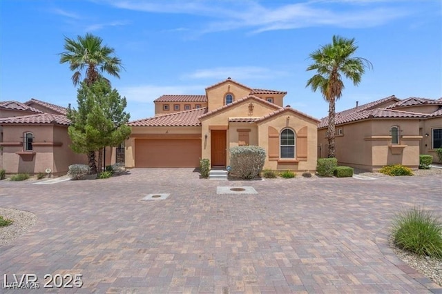 mediterranean / spanish-style home featuring decorative driveway, a tile roof, an attached garage, and stucco siding