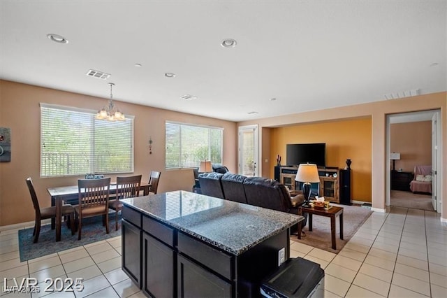 kitchen with light tile patterned floors, stone counters, a notable chandelier, visible vents, and a center island