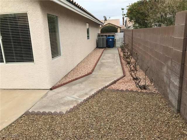 view of side of home featuring a fenced backyard, a tiled roof, cooling unit, and stucco siding