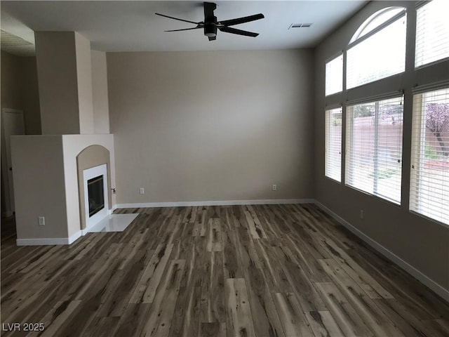 unfurnished living room featuring baseboards, a fireplace with flush hearth, visible vents, and wood finished floors