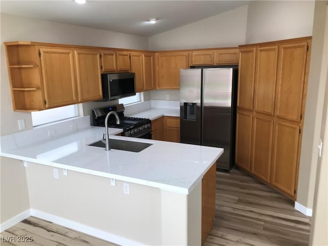 kitchen featuring light wood finished floors, lofted ceiling, a peninsula, stainless steel appliances, and light countertops