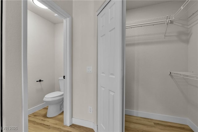 bathroom with a walk in closet, baseboards, toilet, and wood finished floors