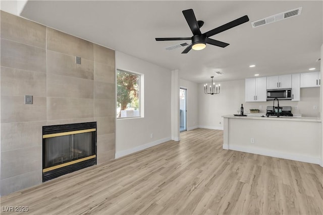 unfurnished living room featuring a tile fireplace, baseboards, visible vents, and light wood finished floors