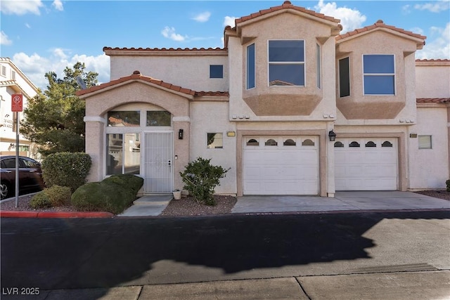 mediterranean / spanish house featuring a garage, a tile roof, driveway, and stucco siding