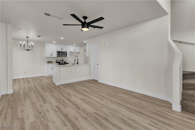 unfurnished living room featuring stairs, light wood finished floors, visible vents, a sink, and ceiling fan with notable chandelier