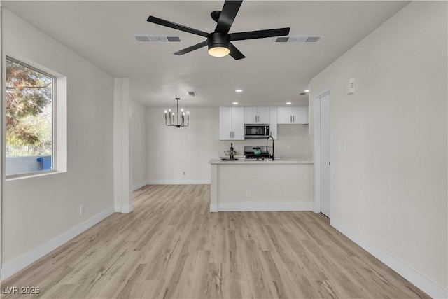 unfurnished living room featuring light wood-style floors, visible vents, baseboards, and ceiling fan with notable chandelier