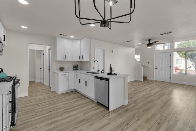 kitchen with stainless steel appliances, a peninsula, a sink, light countertops, and light wood-type flooring