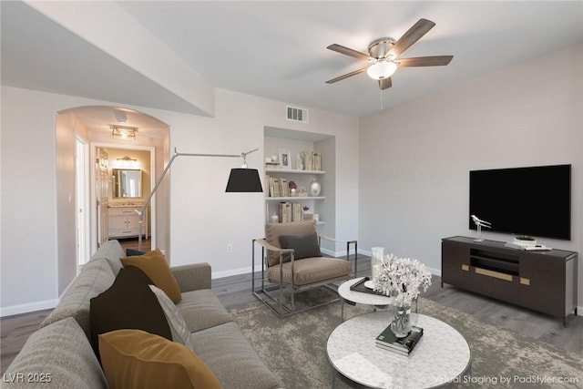 living area with arched walkways, wood finished floors, visible vents, and baseboards