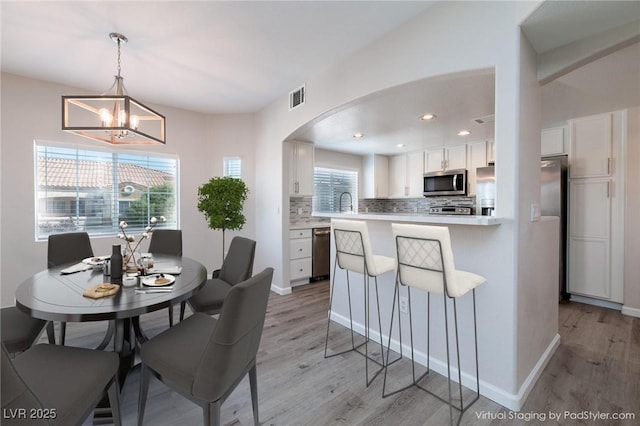 dining room with arched walkways, a notable chandelier, recessed lighting, visible vents, and light wood-style flooring