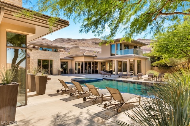 back of property featuring an outdoor pool, a balcony, a patio area, a mountain view, and stucco siding