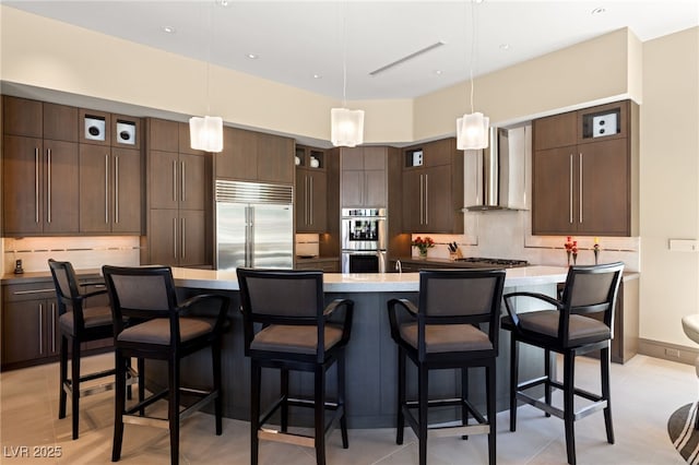 kitchen featuring stainless steel appliances, wall chimney range hood, dark brown cabinets, and tasteful backsplash