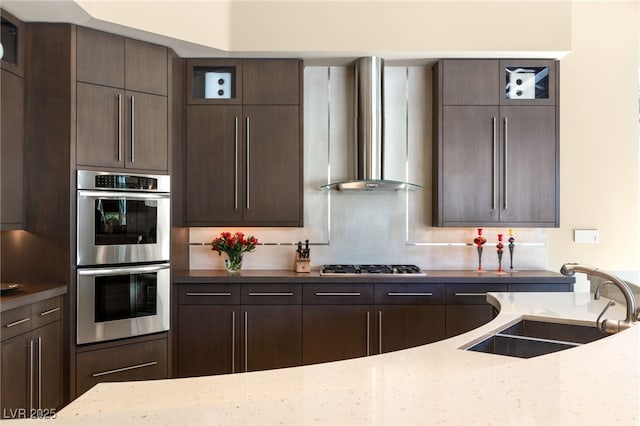 kitchen with stainless steel appliances, dark brown cabinets, wall chimney exhaust hood, and a sink