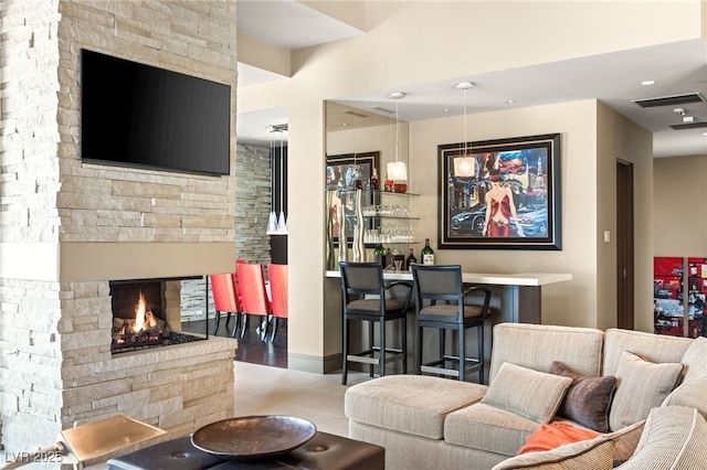 living area with a dry bar, visible vents, and a stone fireplace