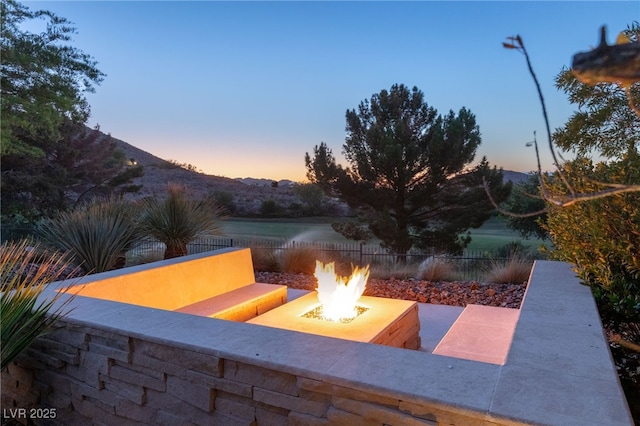 patio terrace at dusk featuring an outdoor fire pit, fence, and a mountain view