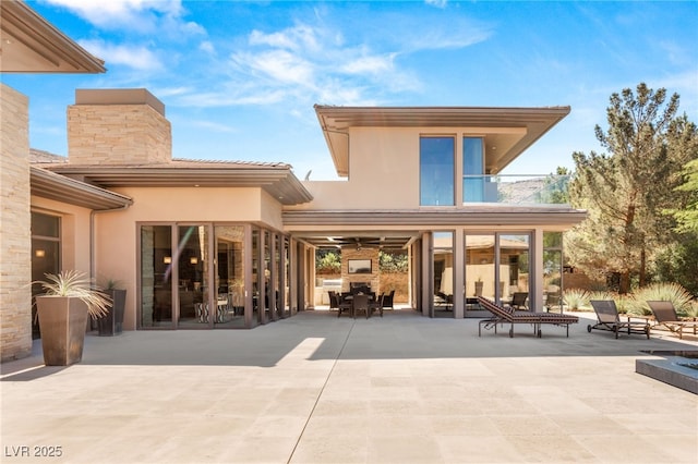 rear view of house with a balcony, stucco siding, a chimney, and a patio