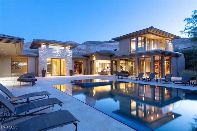 back of property featuring stone siding, an outdoor pool, a patio, and a balcony