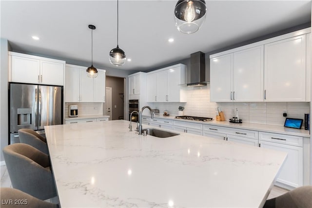 kitchen with a spacious island, wall chimney exhaust hood, appliances with stainless steel finishes, a breakfast bar, and a sink