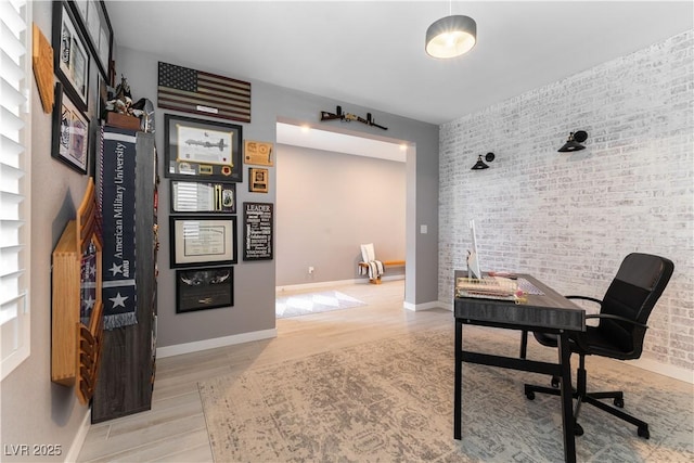 office space with brick wall, wood finished floors, and baseboards